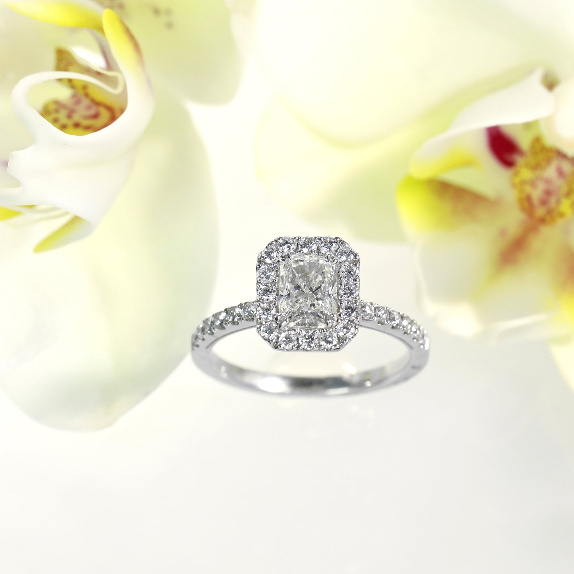 14K white gold diamond engagement ring featuring one rectangular radiant diamond, and a diamond halo and side stones with round brilliant diamonds.