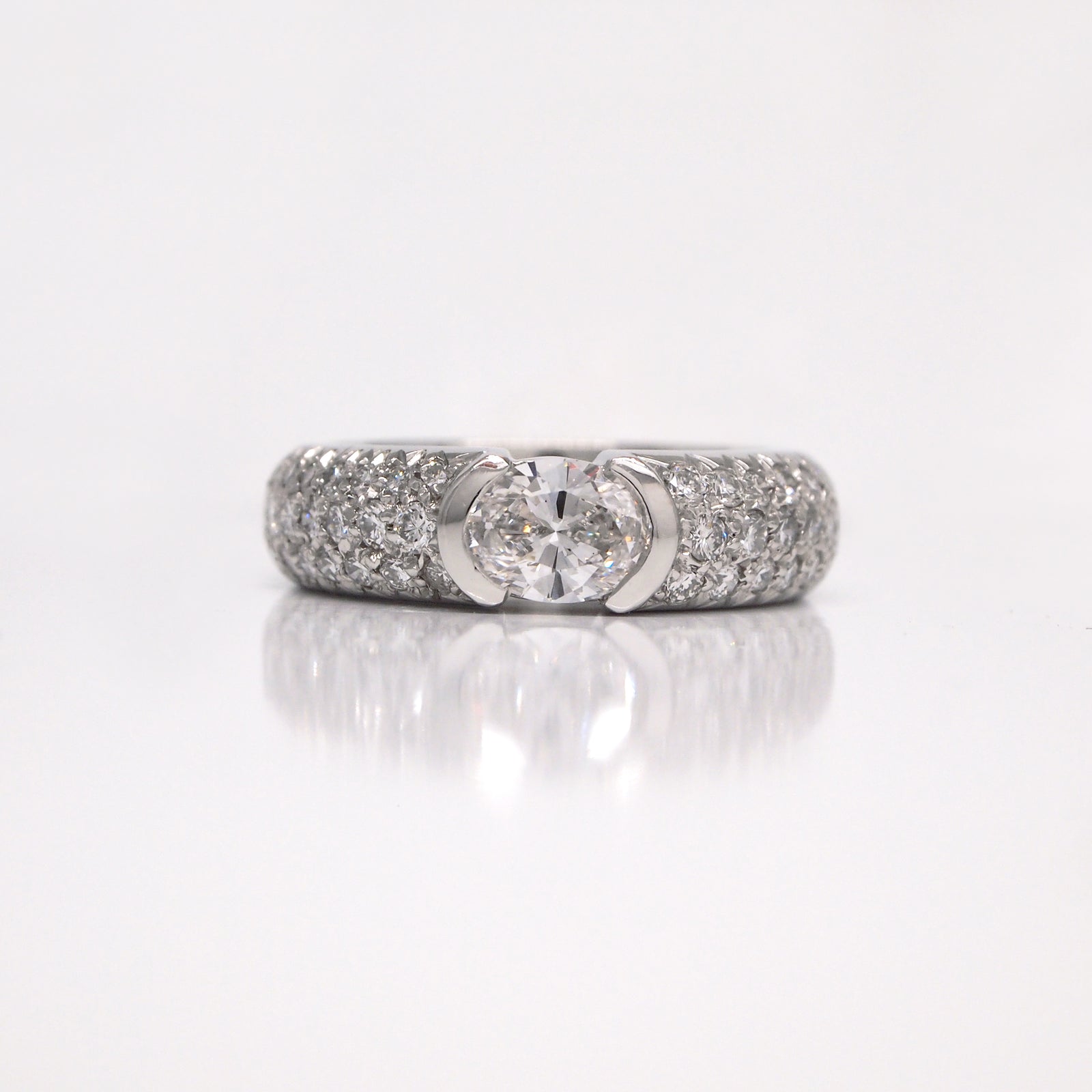 Platinum diamond engagement ring featuring one 0.70 carat oval diamond (SI1, E color), and pave set diamonds weighing a total of 0.75 carats.