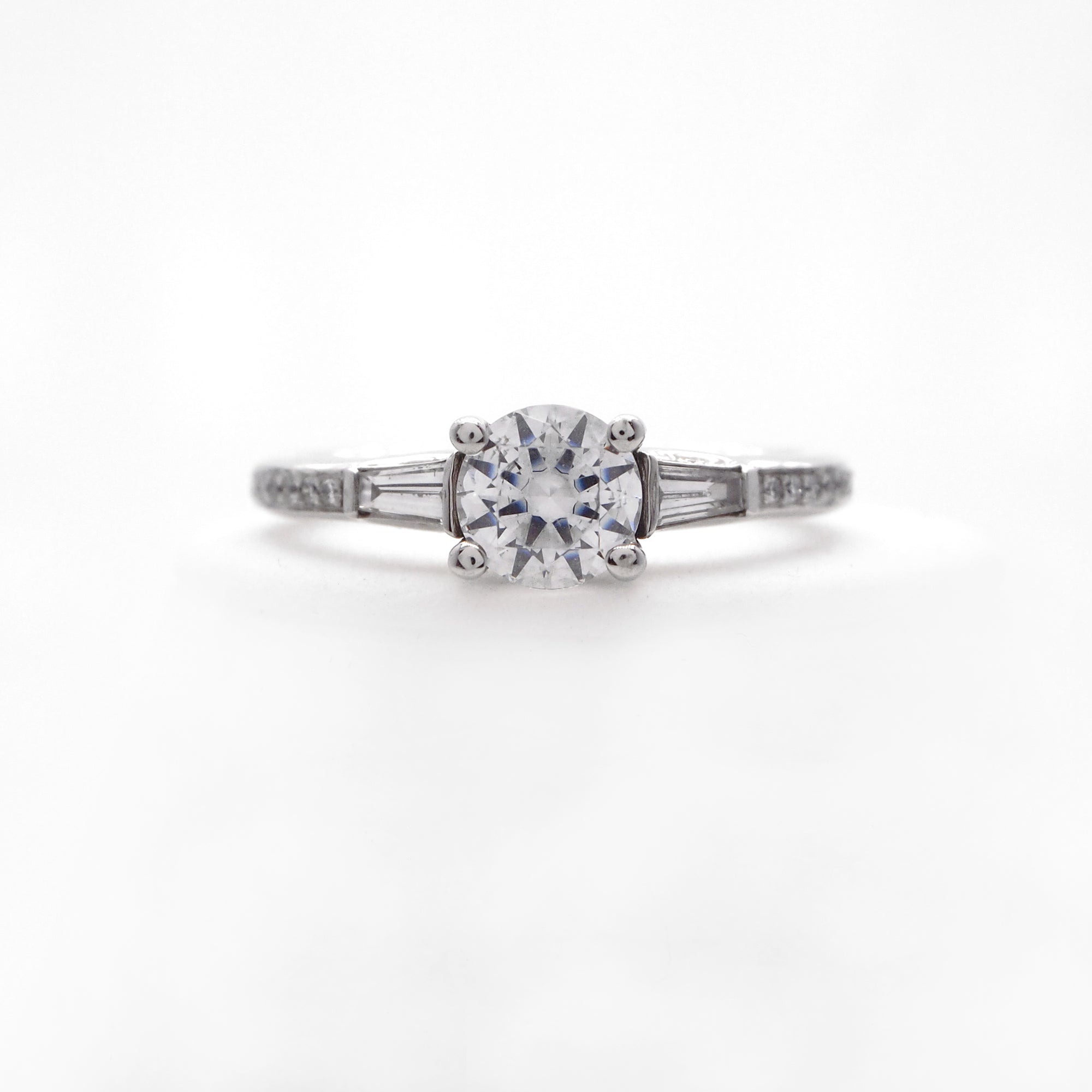 Platinum 3-stone diamond engagement ring featuring two baguette diamonds weighing a total of 0.18 carats, and round brilliant diamonds weighing a total of 0.11 carats. 