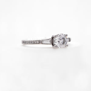 Platinum 3-stone diamond engagement ring featuring two baguette diamonds weighing a total of 0.18 carats, and round brilliant diamonds weighing a total of 0.11 carats. 