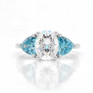 Judith Arnell Jewelers 14K white gold moissanite and zircon ring featuring one 2.00 carat oval moissanite, and 2 trillion-cut blue zircons weighing a total of 2.32 carats set in a 3-stone design.