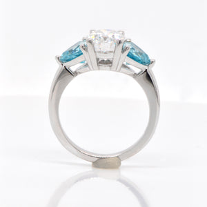 14K white gold moissanite and zircon ring featuring one 2.00 carat oval moissanite, and 2 trillion-cut blue zircons weighing a total of 2.32 carats set in a 3-stone design. Judith Arnell Jewelers