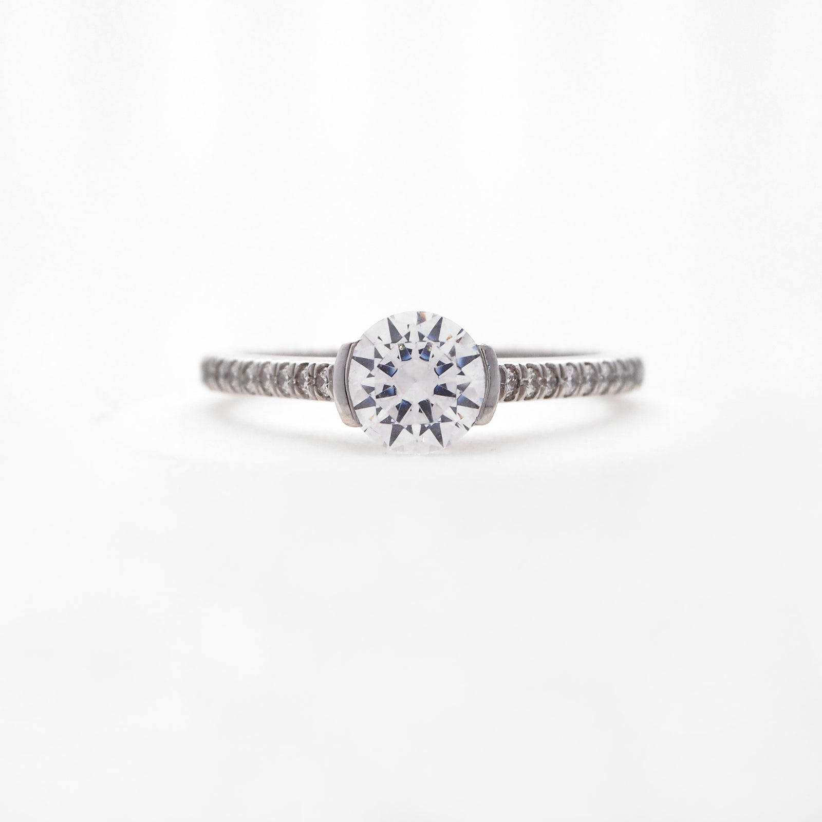 Platinum diamond engagement ring featuring a half bezel center stone setting, and round brilliant diamonds weighing a total of 0.16 carats. 