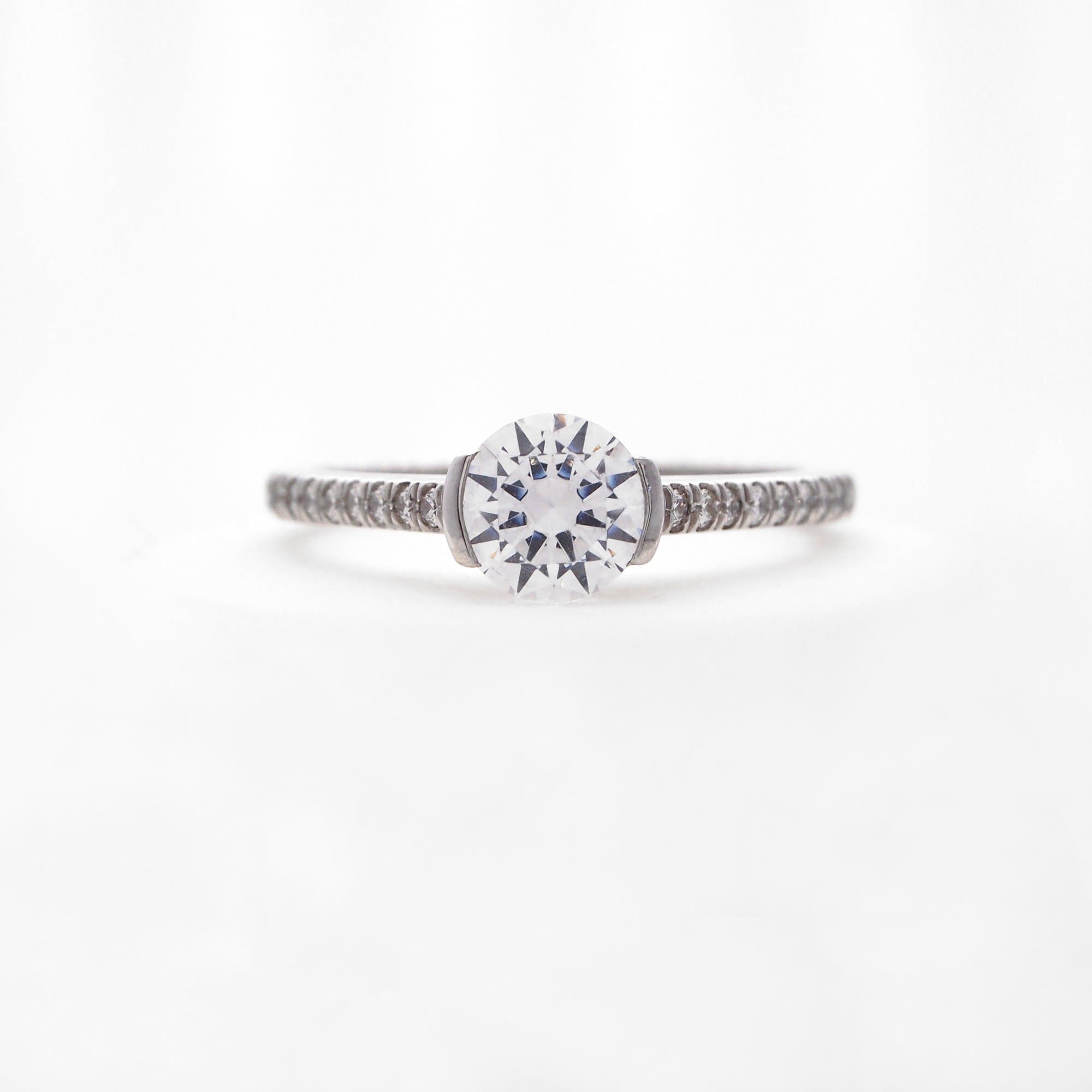 Platinum diamond engagement ring featuring a half bezel center stone setting, and round brilliant diamonds weighing a total of 0.16 carats. 