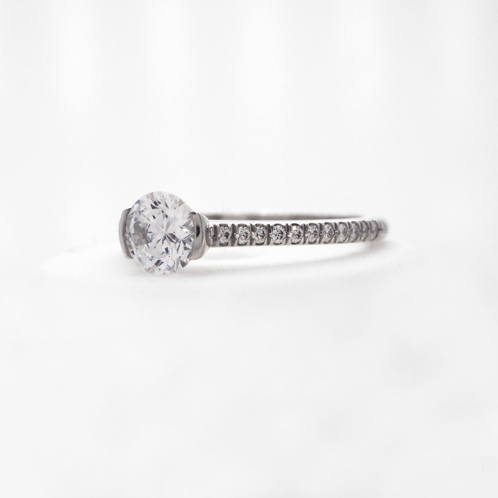 Platinum diamond engagement ring featuring a half bezel center stone setting, and round brilliant diamonds weighing a total of 0.16 carats. 