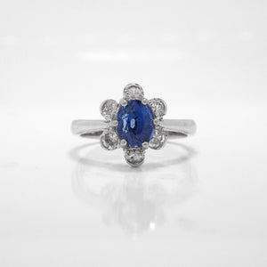 18K white gold sapphire and diamond ring featuring one 1.70 carat oval blue sapphire, and a 6 diamond halo with diamonds weighing a total of 0.56 carats.