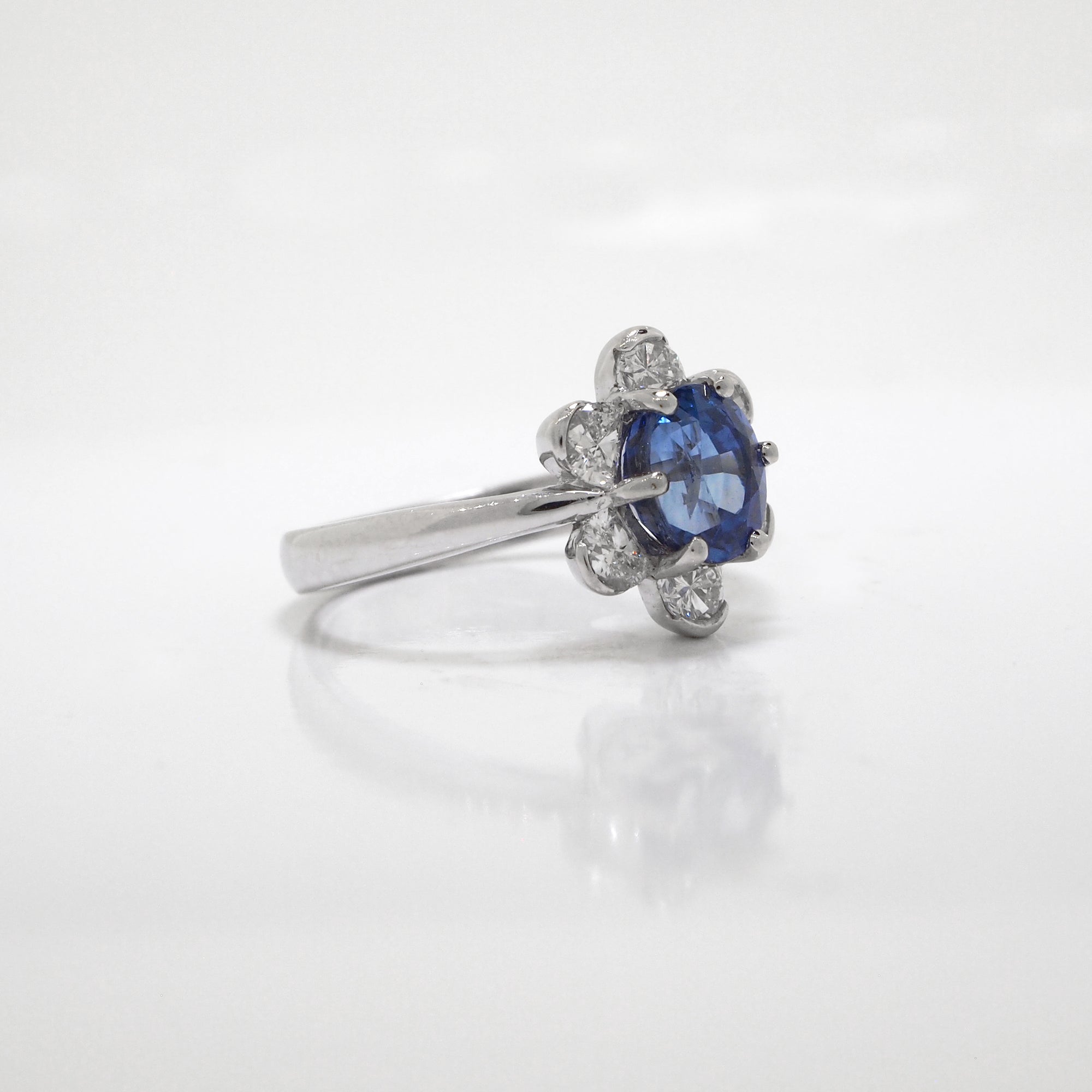 18K white gold sapphire and diamond ring featuring one 1.70 carat oval blue sapphire, and a 6 diamond halo with diamonds weighing a total of 0.56 carats.