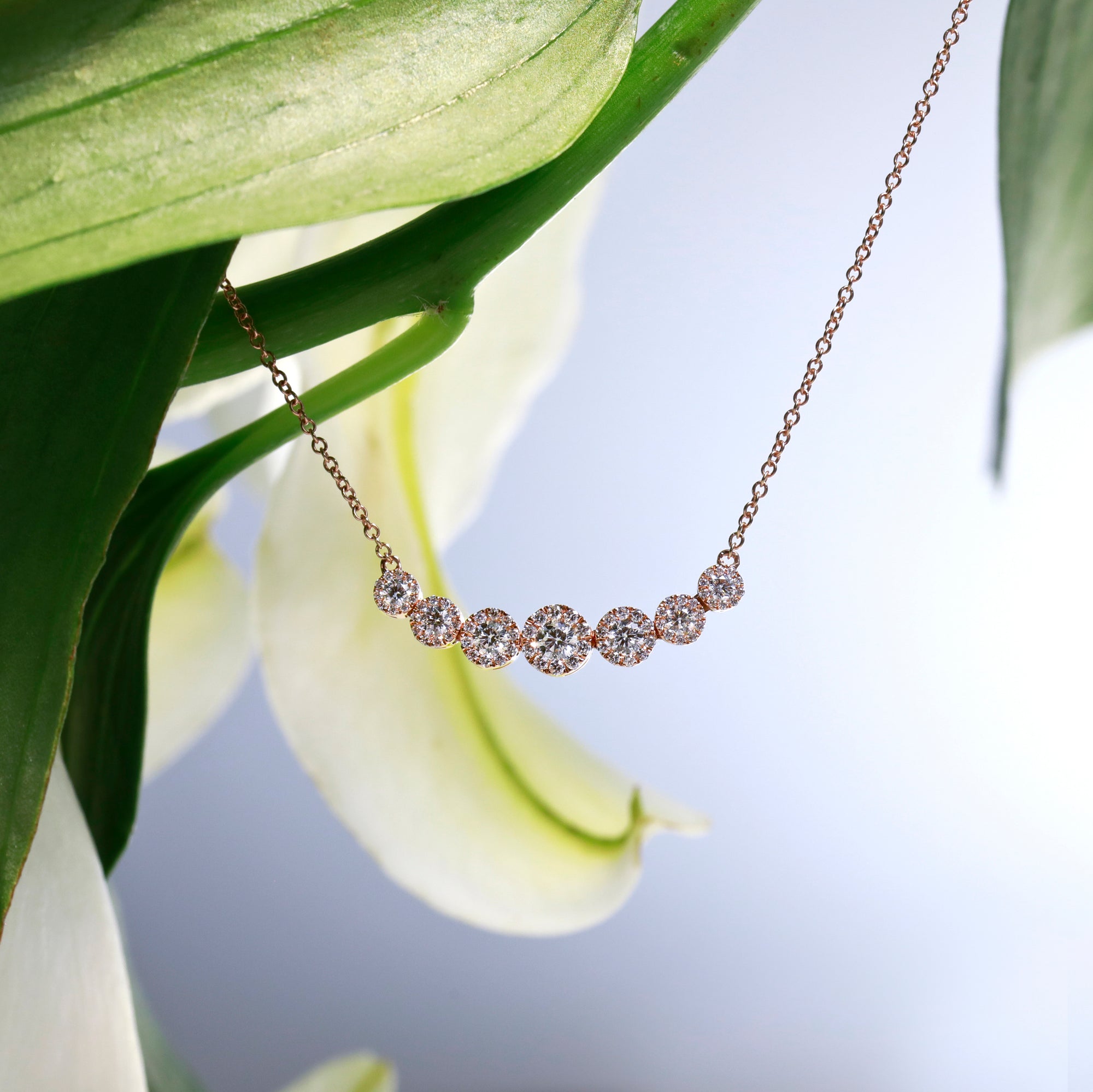 16-inch 14K rose gold diamond necklace featuring 7 round brilliant diamonds with halos set in a graduated design. Diamonds weigh a total of 0.71 carats.