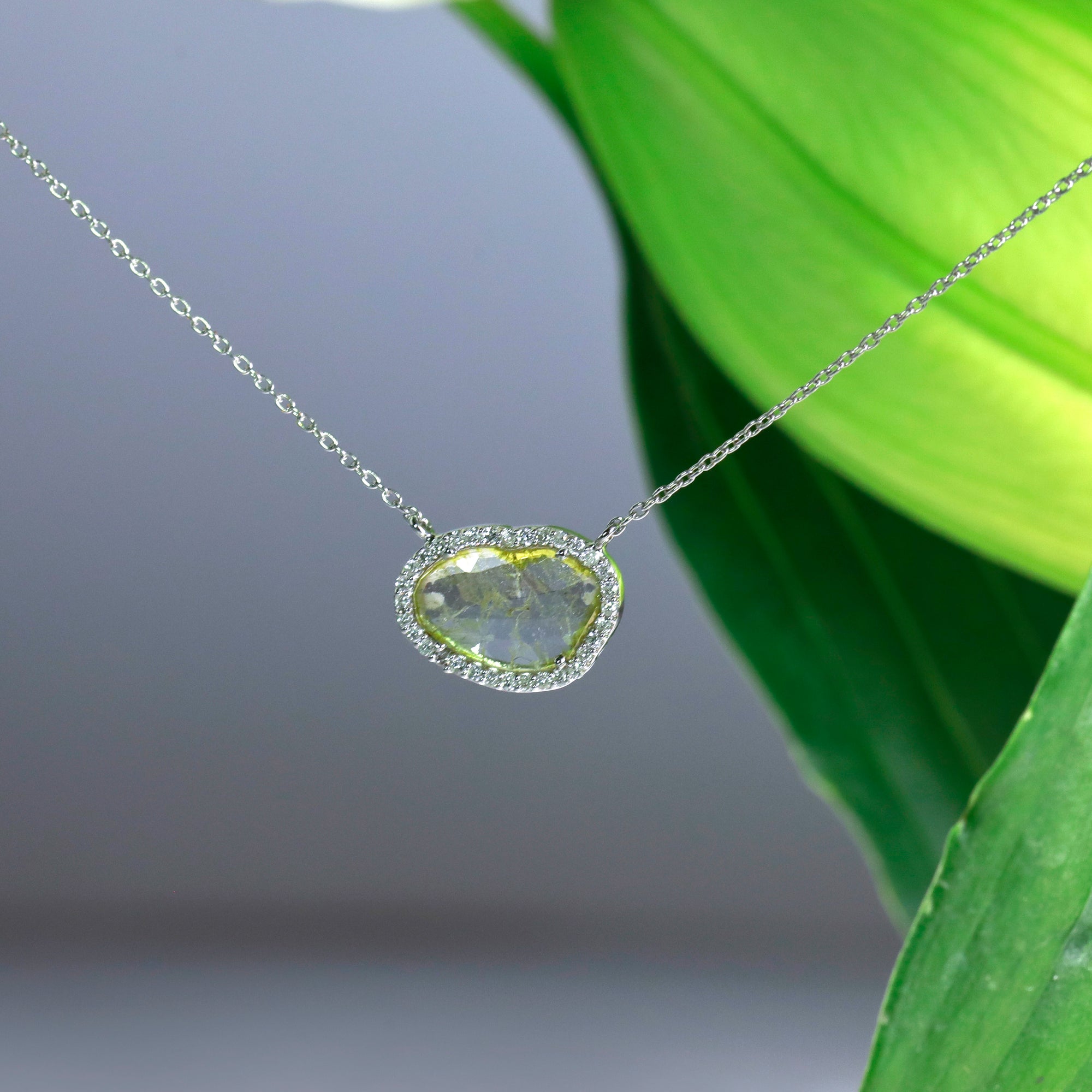 14K white gold diamond necklace featuring one lightly faceted diamond slice weighing 0.60 carats, and a diamonds halo with round brilliant diamonds weighing a total of 0.16 carats.