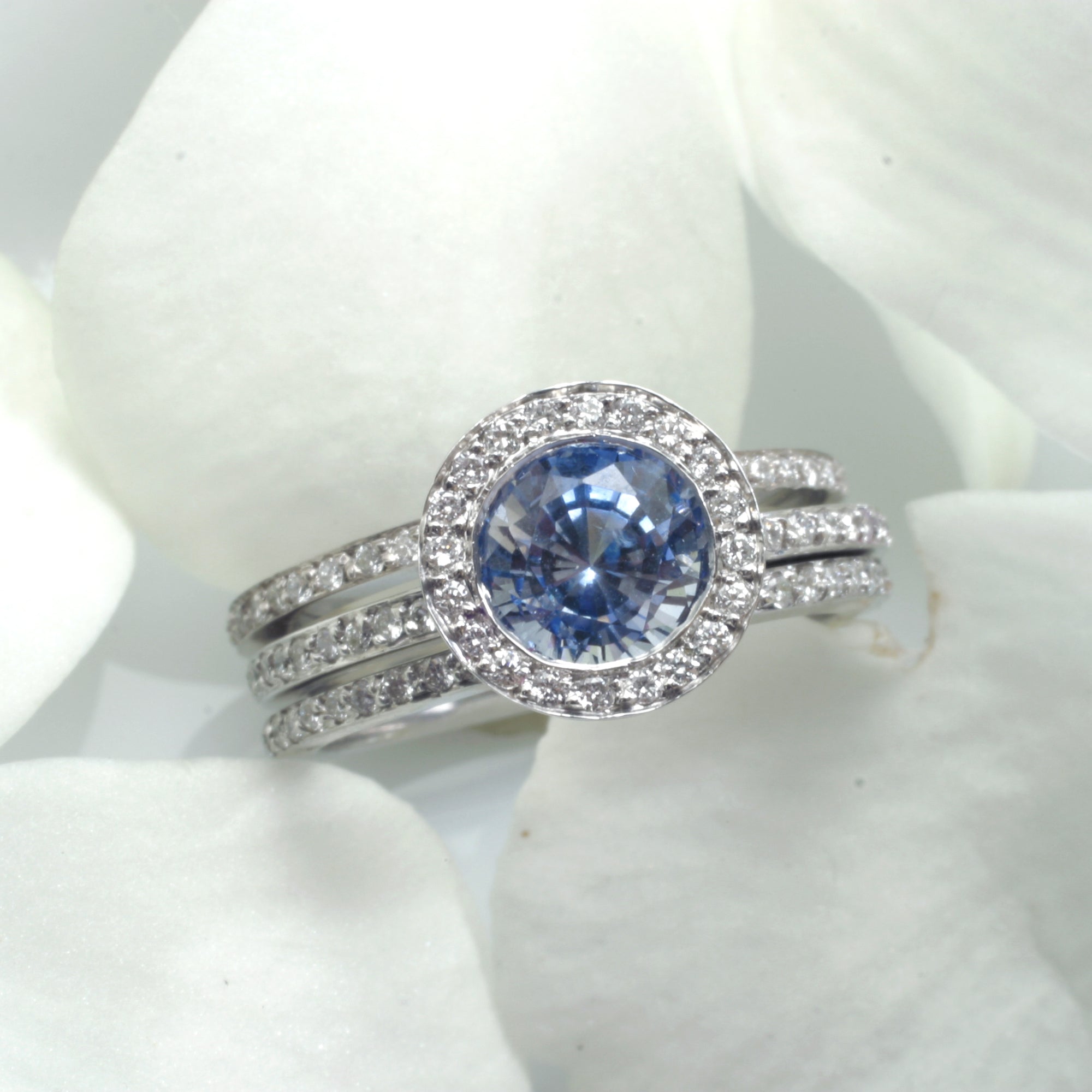 14K white gold sapphire engagement ring featuring 1 round ceylon blue sapphire bezel set in diamond halo in a full diamond eternity design. Available with a matching diamond eternity wedding band (ring guards). Judith Arnell Jewelers
