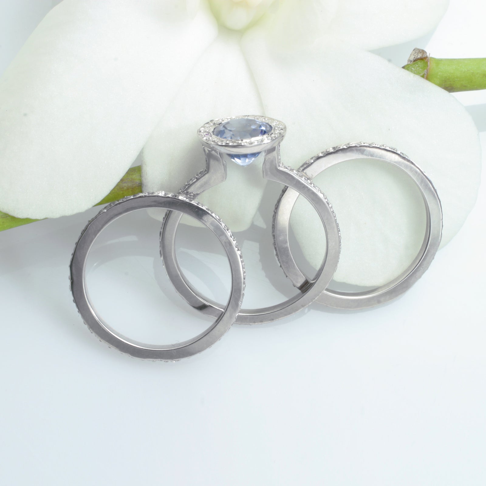 14K white gold sapphire engagement ring featuring 1 round ceylon blue sapphire bezel set in diamond halo in a full diamond eternity design. Available with a matching diamond eternity wedding band (ring guards). Judith Arnell Jewelers