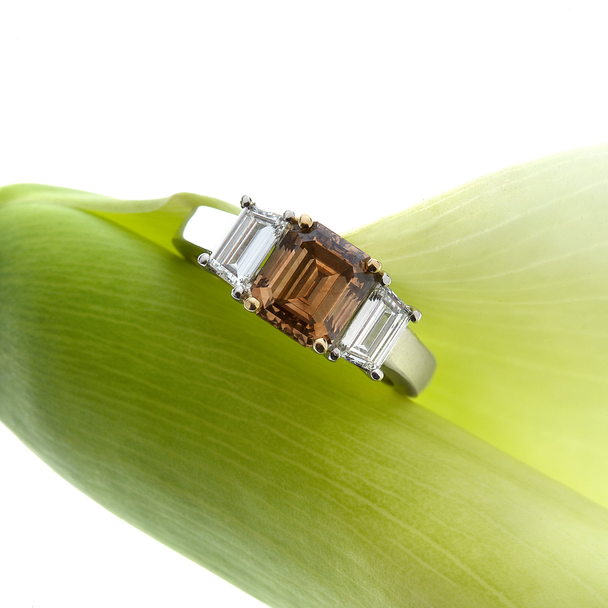 18K gold diamond engagement ring featuring 1 emerald-cut cognac diamond in a 14K yellow gold 4-prong setting, and 2 trapezoid diamonds in a 3-stone design. Judith Arnell Jewelers
