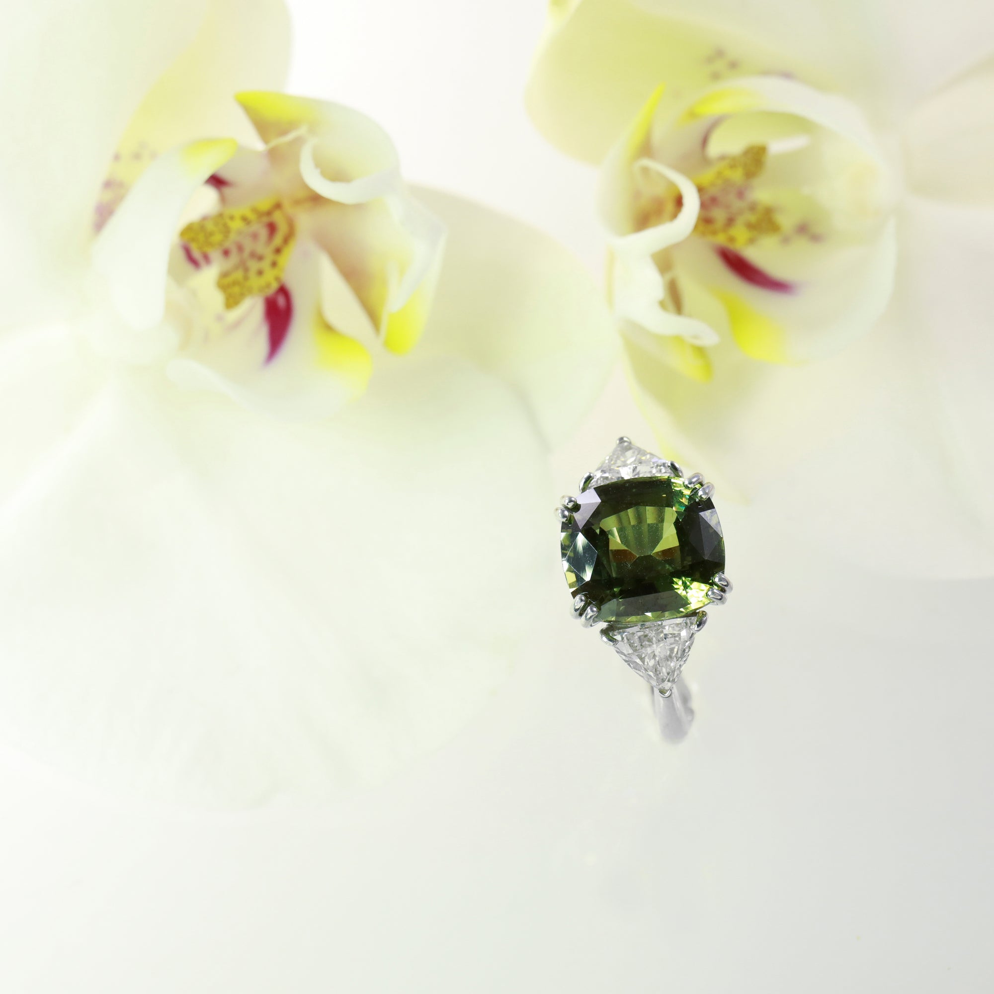 Platinum 3-stone natural sapphire and diamond ring featuring one 7.07 natural green-yellow sapphire, and two trillion diamonds weighing a total of 1.09 carats.