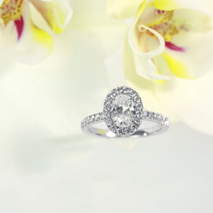 14k white gold diamond engagement ring featuring a 0.84 carat oval diamond center and round brilliant diamond halo and side stones weighing a total of 0.45 carats. Total diamond weight: 1.29ct