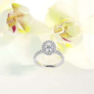14k white gold diamond engagement ring featuring a 0.84 carat oval diamond center and round brilliant diamond halo and side stones weighing a total of 0.45 carats. Total diamond weight: 1.29ctw.
