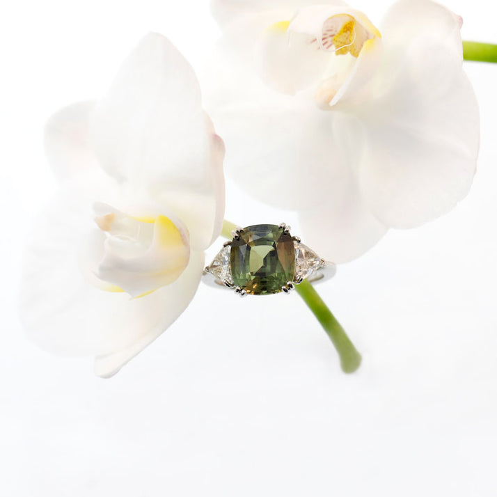 Platinum 3-stone natural sapphire and diamond ring featuring one 7.07 natural green-yellow sapphire, and two trillion diamonds weighing a total of 1.09 carats.