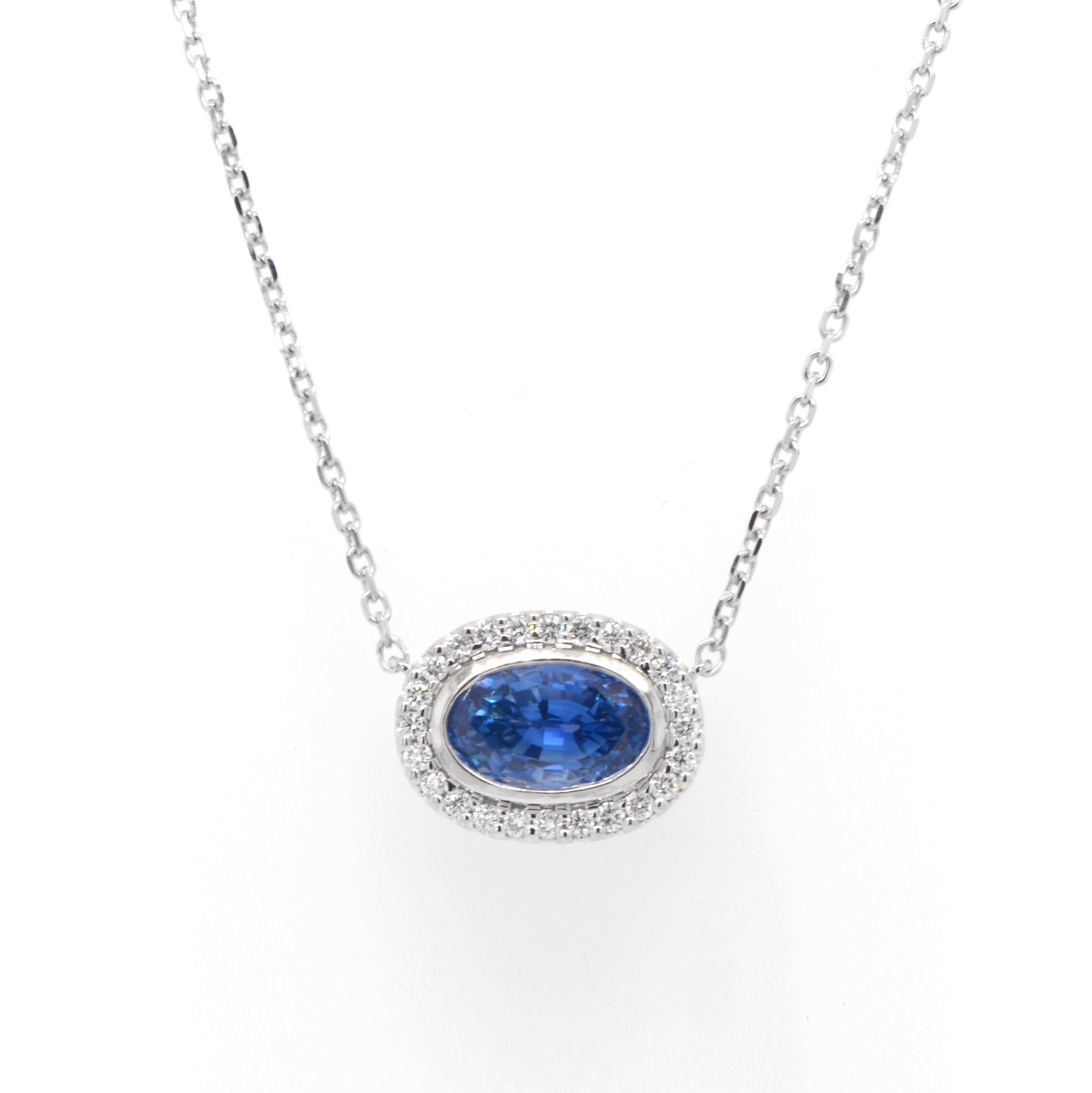 14K white gold sapphire and diamond necklace featuring one 2.90 carat oval blue sapphire set East-West in a diamond halo (0.24ctw).