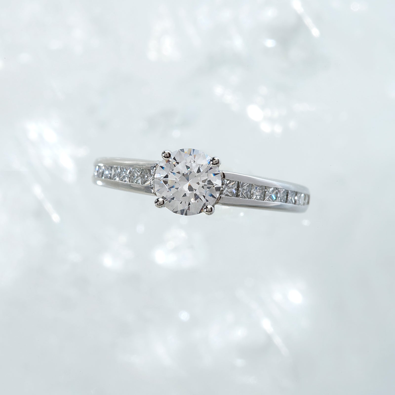 Diamond engagement ring featuring a round brilliant-cut diamond. and channel-set princess-cut diamonds. Custom-made to order for any size diamond or gemstone center stone. Available in 14K or 18K white, yellow, rose gold, and platinum. 